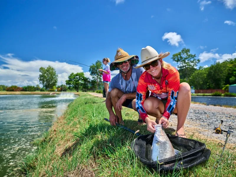 Two people on riverbank with Barramundi