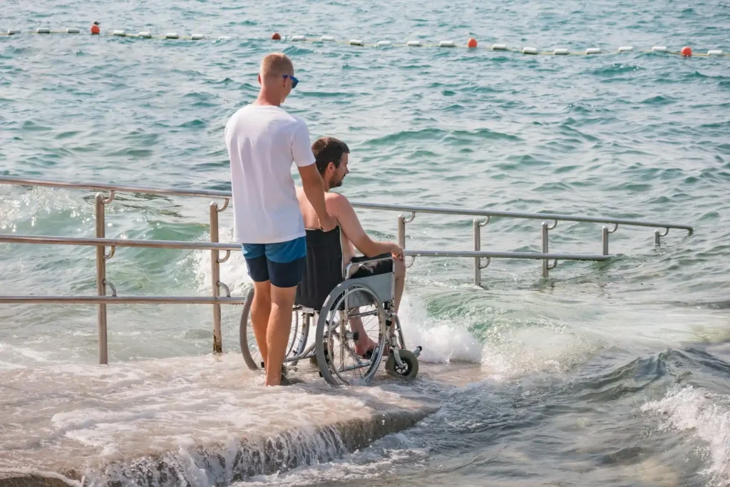 Disabled man in wheelchair with support worker going into the ocean via a ramp